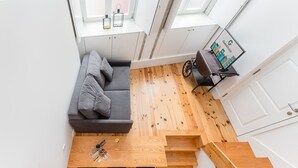 Ein gemütlicher Raum mit grauem Sofa, Holzboden, einem kleinen Tisch mit Zeitschriften und einem Gepäckträger.