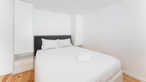Ein schlicht eingerichtetes Schlafzimmer mit Bett, weißen Wänden und Holzboden.