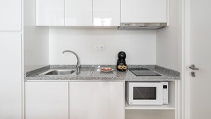 A kitchen with white cabinets, a granite countertop, a stainless steel sink, a black coffee maker, and a white microwave.