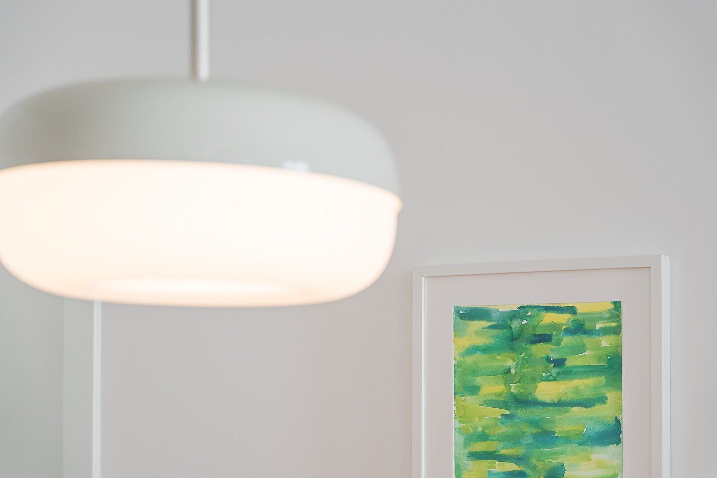 A modern pendant light fixture and a framed abstract painting on a plain wall.