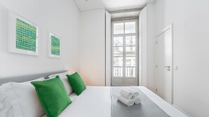 A modern hotel room with a neatly made bed, green pillows, and a view through a glass door.