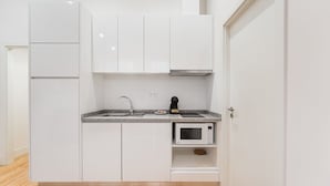 A compact kitchen with white cabinets, a granite countertop, a microwave, and a sink. - GuestReady - Paramount Code Indigo (Porto)