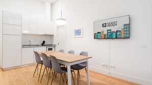 A modern kitchen with white cabinets, a wooden dining table, and grey chairs. - GuestReady - Paramount Code Indigo (Porto)