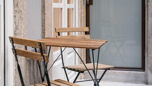 A set of wooden folding chairs with metal legs, positioned against a textured wall with a window in the background. - GuestReady - Paramount Code Indigo (Porto)