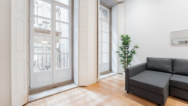 A modern living room with a grey sofa, a large window with multiple panes, and a potted plant. - GuestReady - Paramount Code Indigo (Porto)