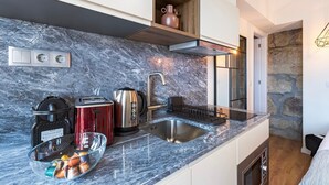 A modern kitchen with a marble countertop, stainless steel appliances, and a stone wall. - GuestReady - Caldeireiros Building (Porto)