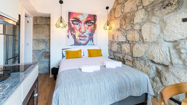 Un dormitorio moderno con pared de piedra, una cama con ropa de cama blanca y amarilla, y lámparas colgantes.