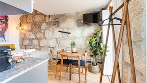 A cozy room with a stone wall, a wooden table with chairs, a TV mounted on the wall, and a painting on the wall. - GuestReady - Caldeireiros Building (Porto)