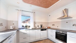 A modern kitchen with white cabinets, a stainless steel range hood, and a window with curtains.