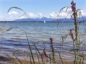 Un paysage côtier offrant une vue dégagée sur la mer, des montagnes lointaines et un voilier.