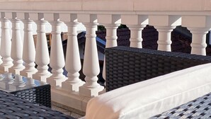 A balcony with white balustrades, wicker furniture, and a white cushion.