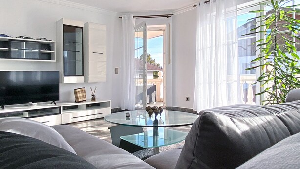 A modern living room with a flat-screen TV, a glass coffee table, and a sofa.
