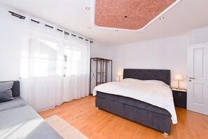 Une chambre à coucher avec un grand lit, une table de chevet avec des lampes, une armoire et une fenêtre avec des rideaux légers.