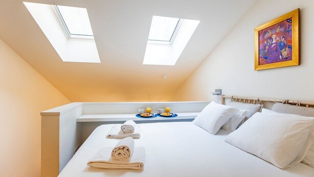 A hotel room with a bed, two skylights, a breakfast tray, and a painting on the wall.