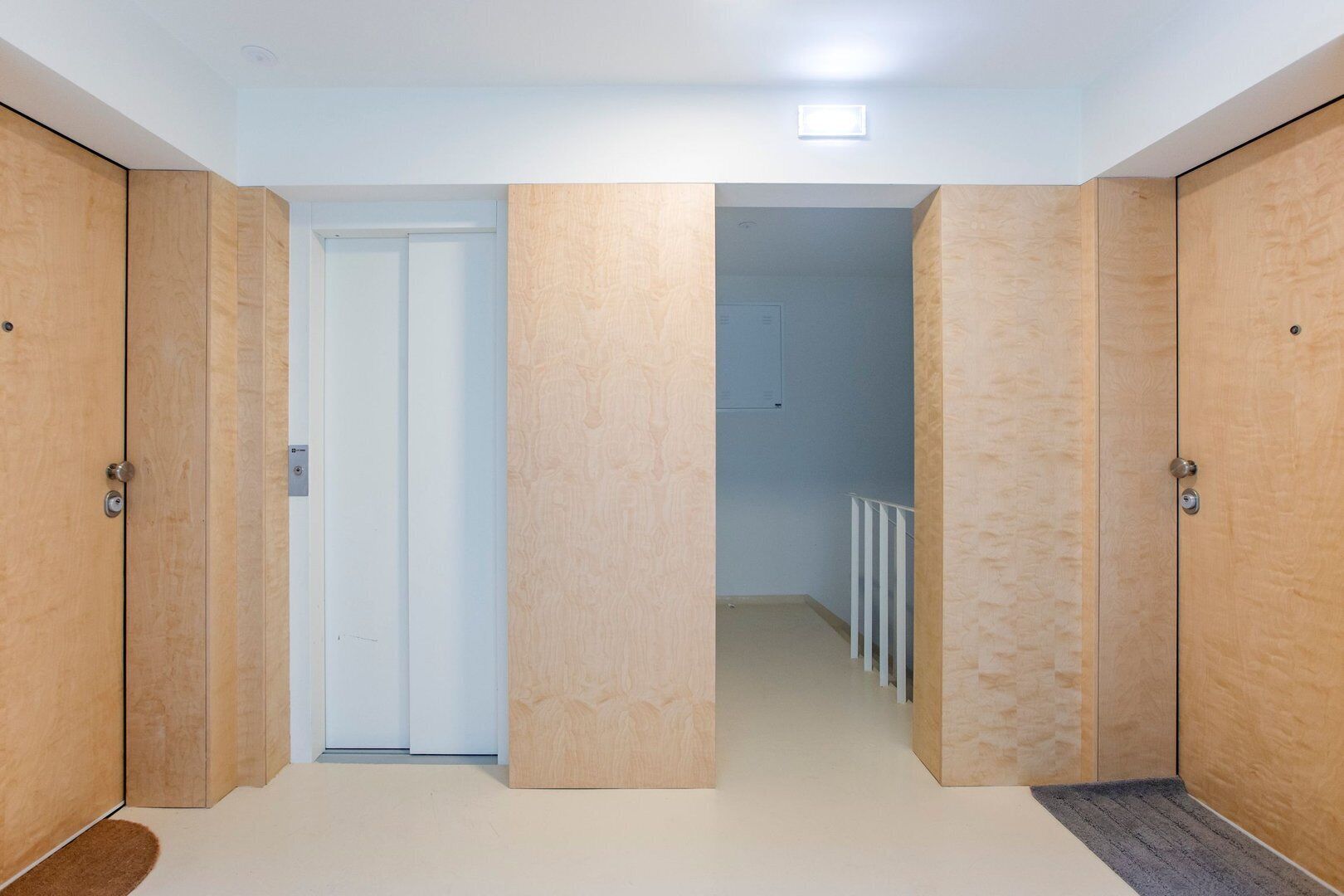 Un pasillo con puertas de madera, una puerta blanca al fondo y un radiador en la parte posterior.