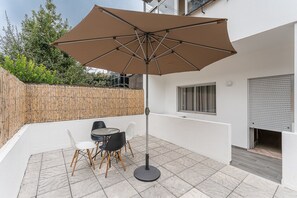 Um pátio com uma mesa, cadeiras, um grande guarda-sol e um cercado de bambu.