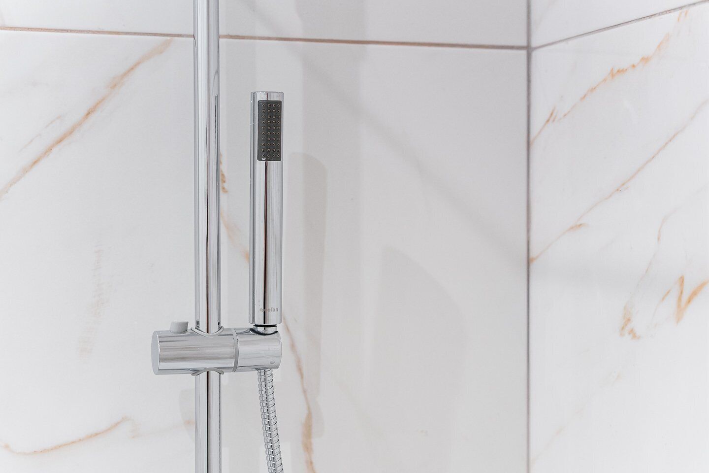 A modern shower with a handheld control and a flexible hose.