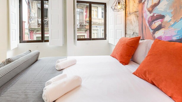 A hotel room with a bed, two windows, a painting, and a hanging light fixture. - GuestReady - Caldeireiros Building (Porto)