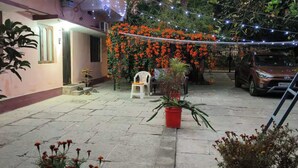 Un patio con un coche aparcado a la derecha, una silla y una planta en maceta en el centro.
