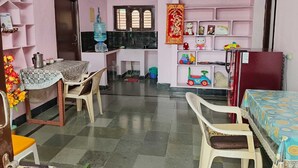 Una habitación con una mesa de comedor, sillas, un refrigerador, un dispensador de agua y estantes con diversos objetos.