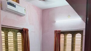 Una habitación pequeña con cama individual, paredes rosas, ventilador de techo y aire acondicionado.