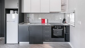 A modern kitchen with grey cabinets, a white refrigerator, a built-in oven, and a granite countertop. - GuestReady - Olivieri's House - 6 (Porto)