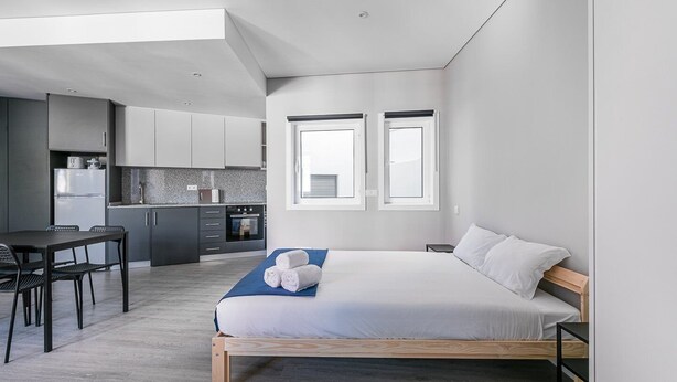 A modern bedroom with a wooden bed, a small desk, and a kitchenette in the background. - GuestReady - Olivieri's House - 6 (Porto)