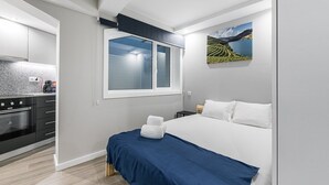 Un dormitorio moderno con una cama grande, una ventana y una cocina visible al fondo.