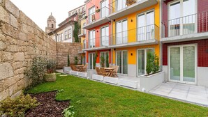 Ein modernes Mehrfamilienhaus mit Mauerwerk, einem kleinen Garten und Sitzmöglichkeiten im Freien.
