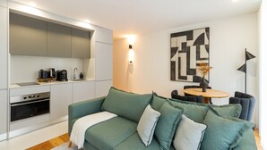 Eine moderne Küche mit Einbaugeräten, eine Essecke mit rundem Tisch und Stühlen sowie ein grünes Sofa mit Kissen.