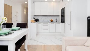 A modern kitchen with white cabinets, a marble countertop, and a dining area with a white table set for two.