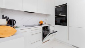 A modern kitchen with white cabinetry, a built-in oven, a dishwasher, and a wooden cutting board.
