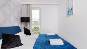 A hotel room with a bed, a black floor lamp, a window with a view, and a painting on the wall.