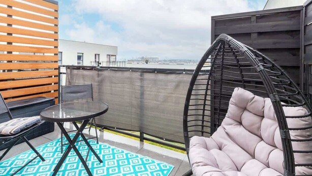 A rooftop terrace with a hanging chair, a small table, and a patterned rug.