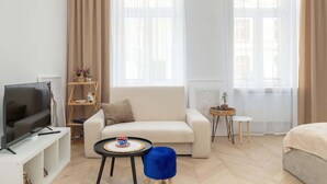 A modern living room with a flat-screen TV, a white sofa, a blue ottoman, and a small side table with a lamp. - Comfortable Studio in the Center of Katowice | For 3 People (Katowice)