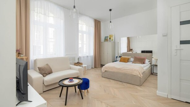 A modern hotel room with a sofa, a small round table, a bed with a headboard, and a television. - Comfortable Studio in the Center of Katowice | For 3 People (Katowice)