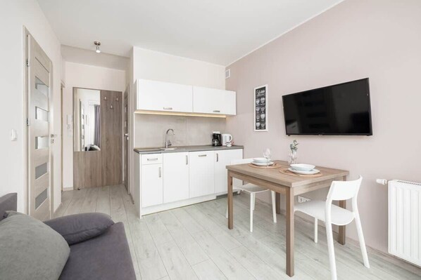 A compact living space with a kitchenette, a dining area, and a TV mounted on the wall.