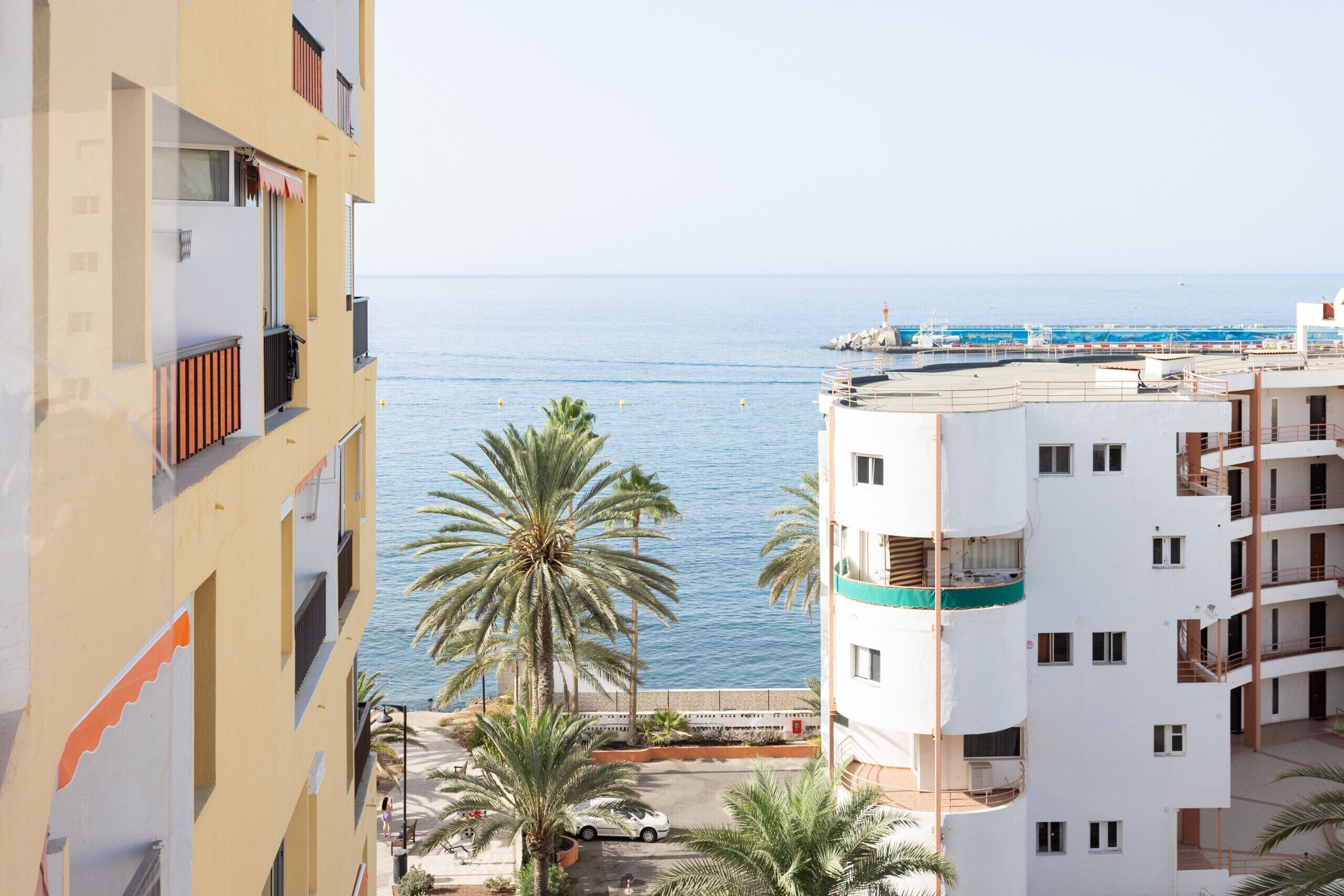 Un edificio costero con balcones que dan al mar, palmeras y un cielo despejado.