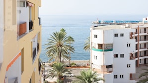 Un bâtiment situé sur la côte, doté de balcons donnant sur la mer, bordé de palmiers et surplombant un ciel dégagé.