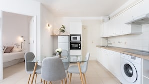 Une cuisine moderne avec une table à manger en verre, des chaises grises, un lave-linge et un four à micro-ondes.