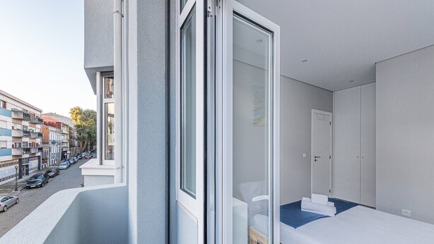 A modern hotel room with a balcony, a bed, a chair, and a wardrobe. - GuestReady - Olivieri's House - 7 (Porto)