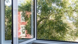 Une fenêtre donnant sur un bâtiment en briques rouges et sur un feuillage verdoyant.