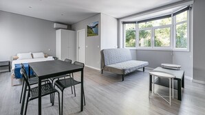 Une pièce moderne et bien éclairée, comprenant une table à manger, des chaises, un canapé et une fenêtre donnant sur un paysage verdoyant.