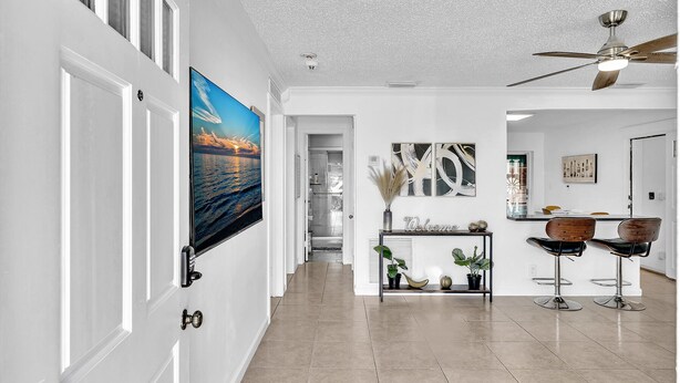 A modern interior with a hallway leading to a dining area, featuring a ceiling fan, a TV, and a welcome sign.