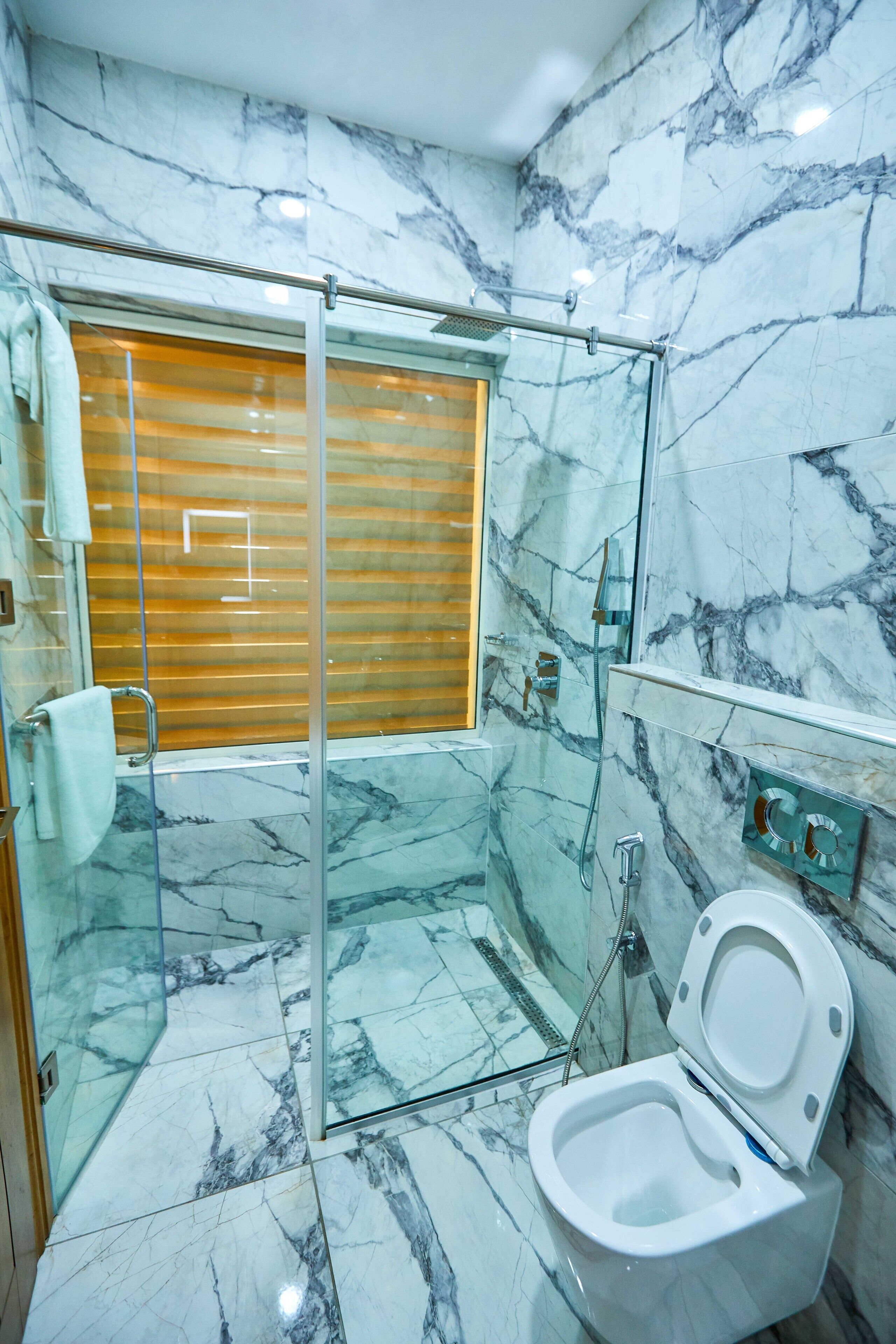 A bathroom with a glass shower enclosure, a toilet, and a marble floor.