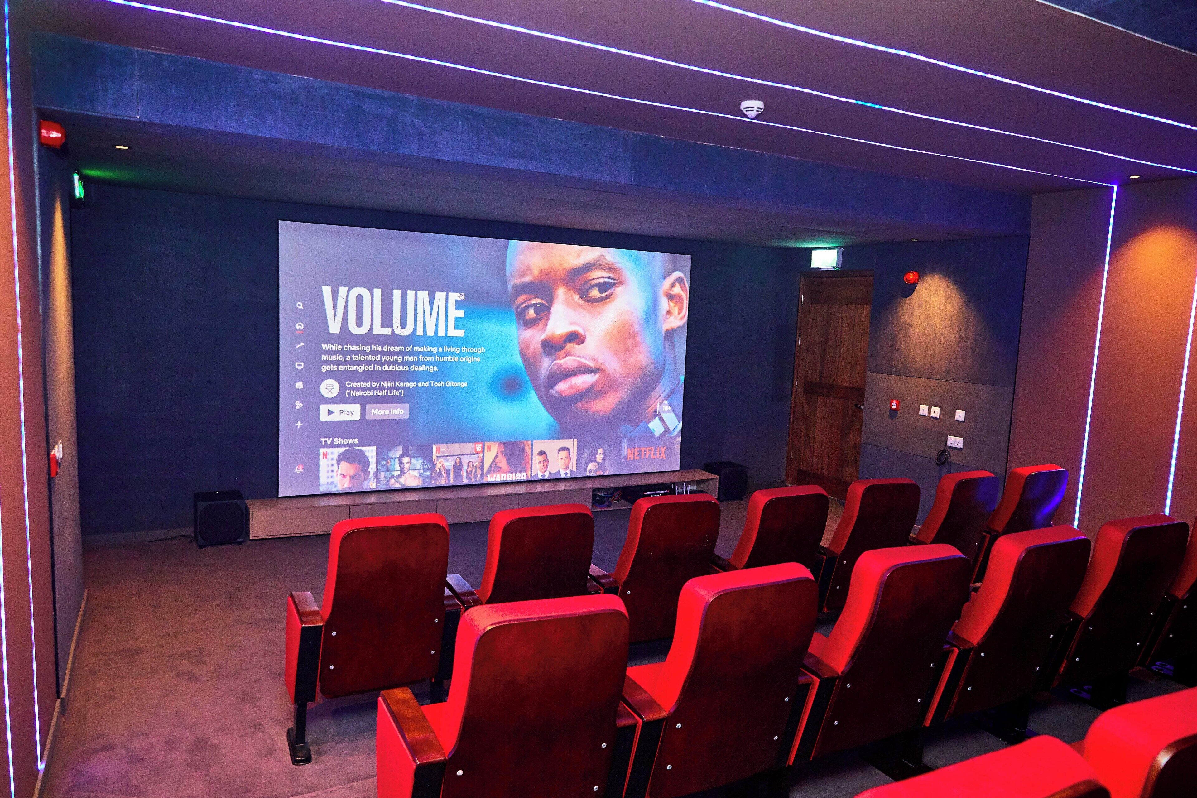 Ein Theater mit Reihen roter Sitze und einer großen Leinwand, die eine Präsentation mit dem Titel 'VOLUME' zeigt.