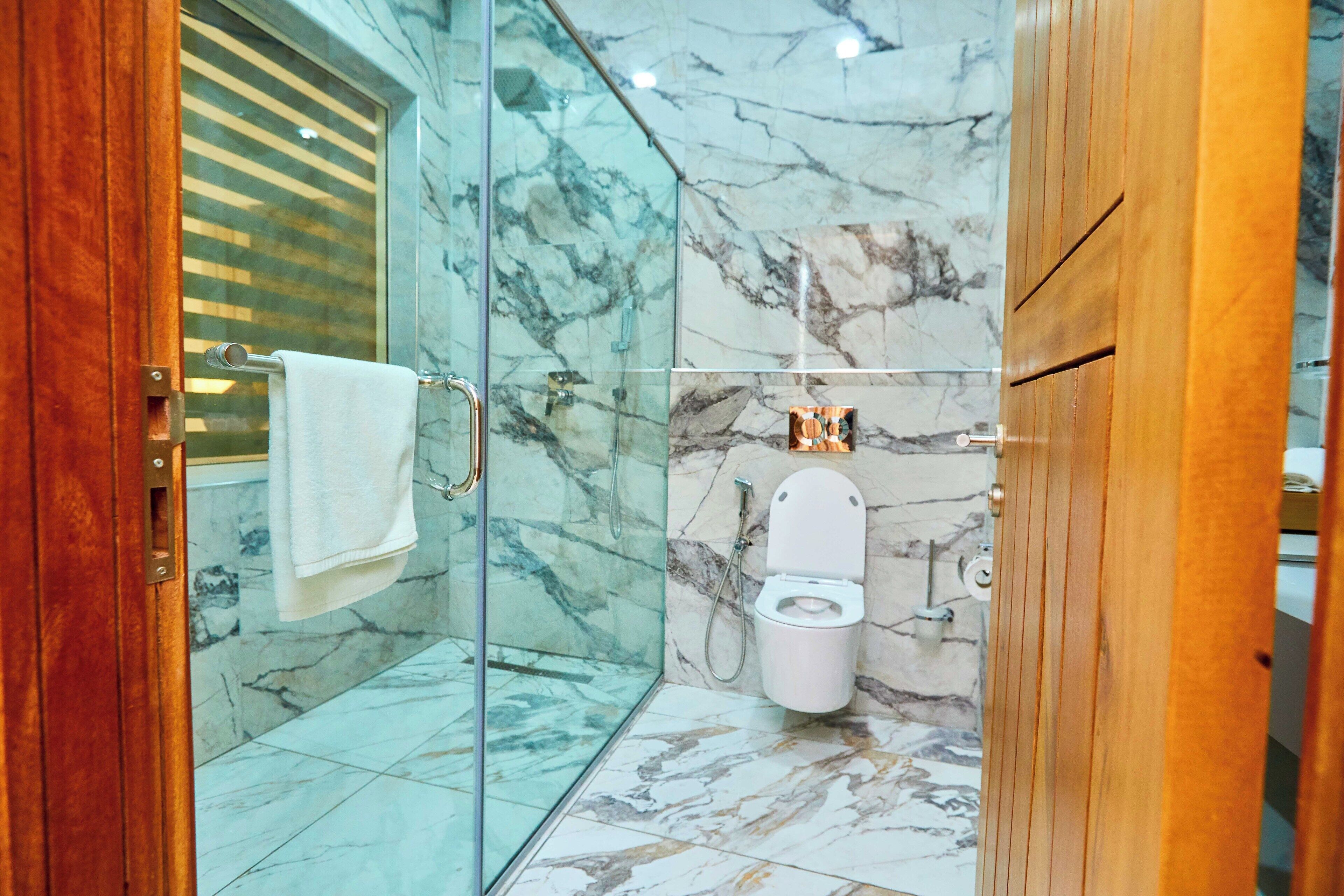 A bathroom with a glass shower enclosure, a marble-tiled floor, and a white toilet.
