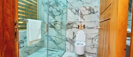 A bathroom with a glass shower enclosure, a marble-tiled floor, and a white toilet.