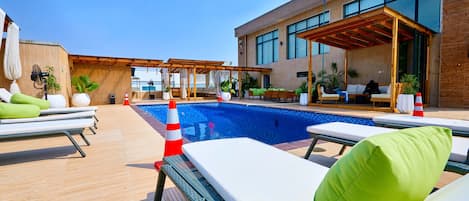 Un área de piscina en la azotea con sillones, una piscina y un edificio moderno con amplias ventanas.