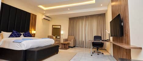 A modern hotel room with a large bed, a desk, a chair, a flat-screen TV mounted on the wall, and a large window with curtains.
